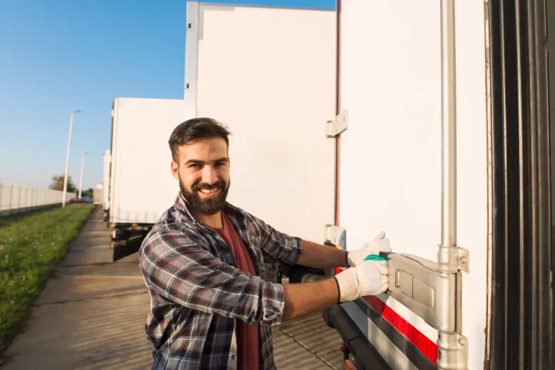 Smiling truck driver closing truck trailer back doors checking goods transportation